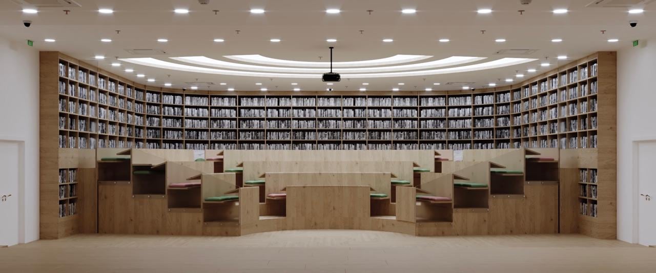 Curved reading room with full-height bookshelves and built-in bench seating either side of a central lecture area