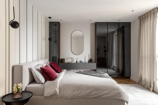 Bedroom of the Dubai Marina apartment by Anna Arsentyeva: fluted upholstered headboard, oval wall mirror, smoked-glass wardrobe fronts, burgundy accent cushions