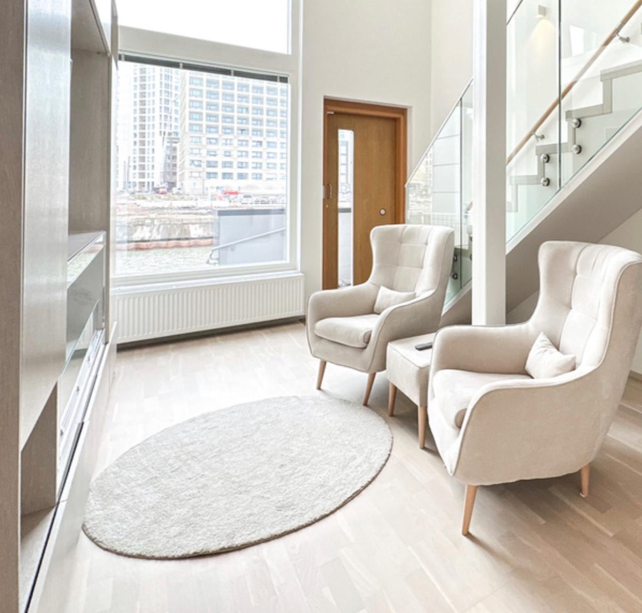 Entryway with two cream wingback armchairs, a round rug, and a harbour view through the floor-to-ceiling window