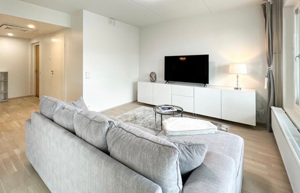 Living room with a grey sectional sofa facing a wall-mounted television and low white media console