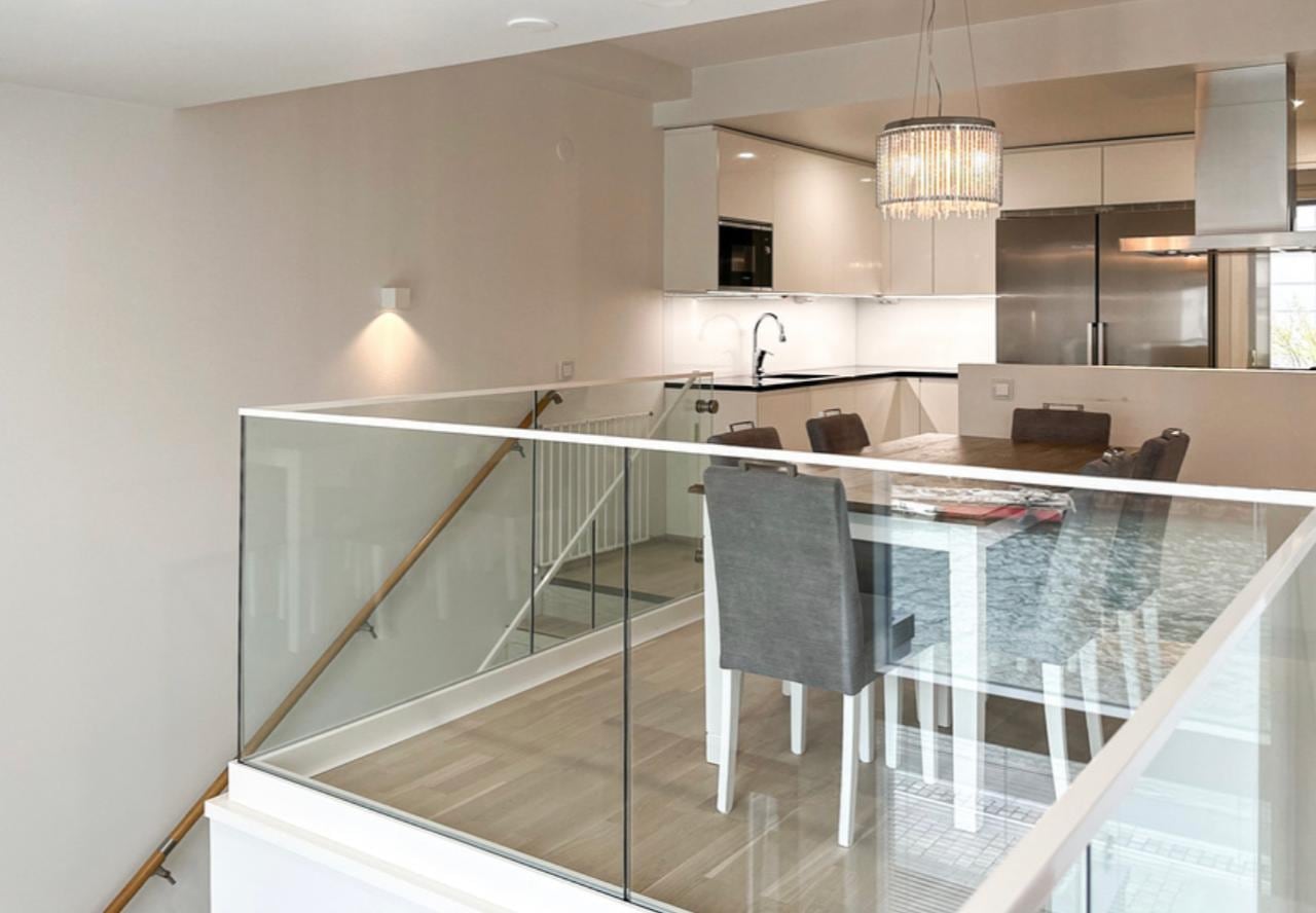 View from the mezzanine over the glass balustrade down to the kitchen and dining table beneath a crystal pendant light