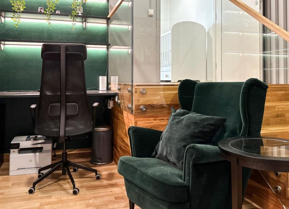 The Emerald Apartment by Anna Arsentyeva: forest-green wing armchair, glass side table, open-tread oak staircase behind glass balustrade