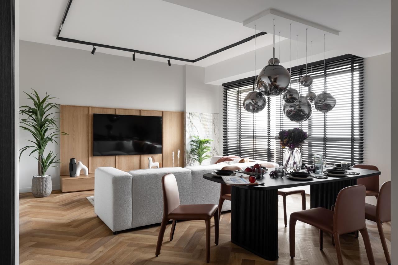 Living room with a boucle sofa, timber-panelled media wall and a dining table beneath a cluster of smoked-glass pendant lights