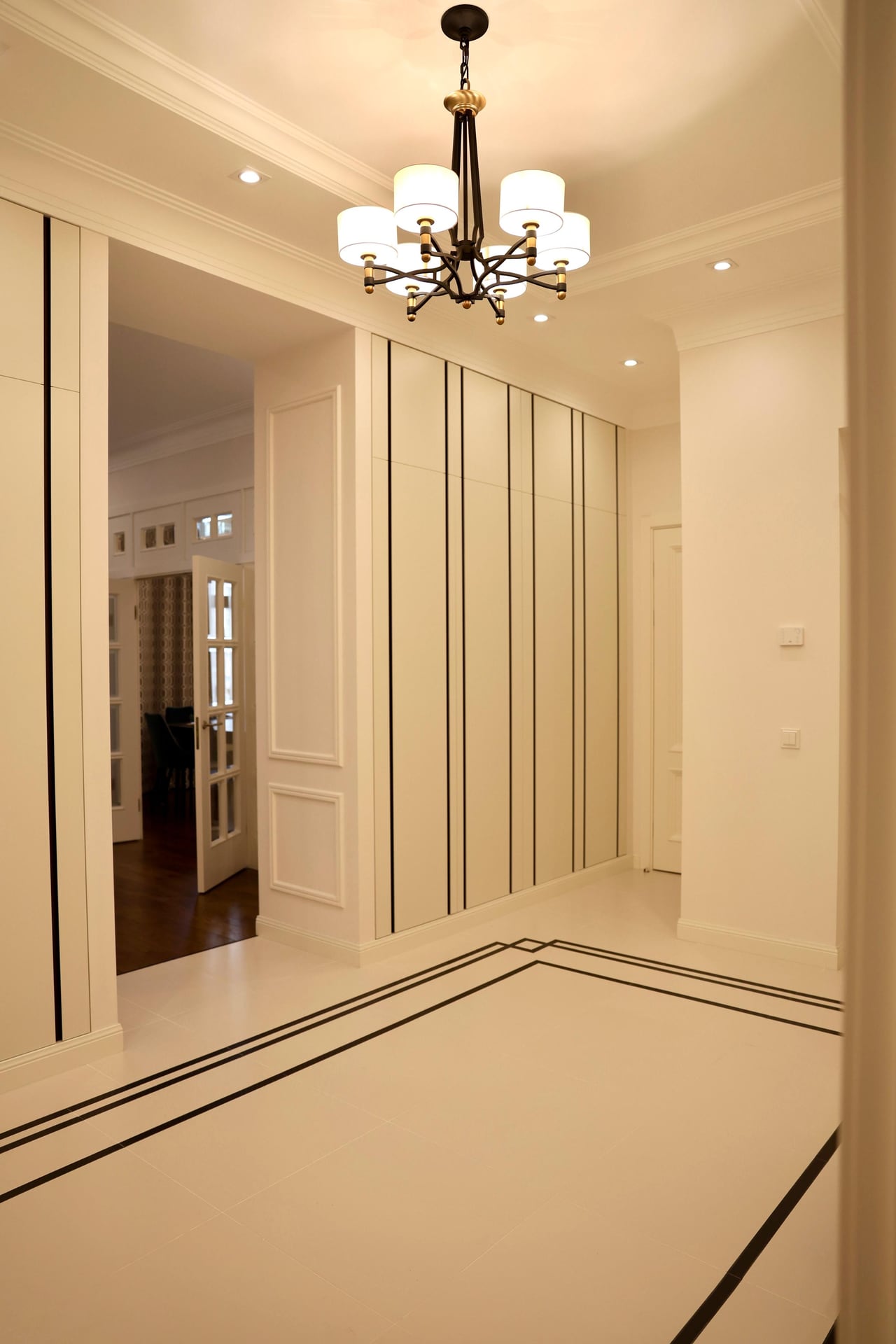 Hallway with a full-height wardrobe wall, inlaid marble-effect floor and a five-arm chandelier