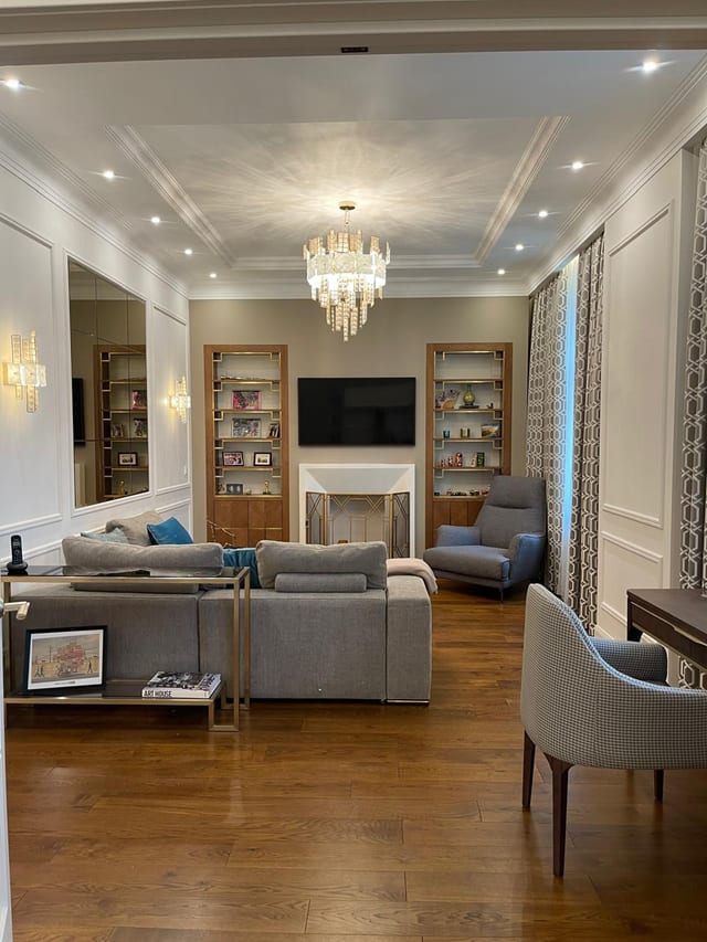 Living room of the Pargolovo country house by Anna Arsentyeva: crystal chandelier, built-in oak shelving either side of the fireplace, herringbone floor