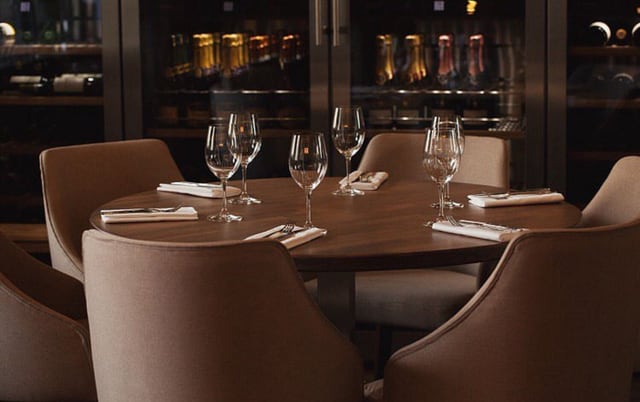 Private dining table set for six by Anna Arsentyeva, with a backlit glass wine cabinet behind it